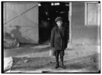 Lewis Hine child labor: Monongah Glass Co., Fairmont, W. Va. Jo Before a glass wks boy going home, 5 P.M. He says he is 12 years old, and has been at it one year: is a "ketchin-up-boy" $.70 a day: says glass business is all right. Asked if he was going to be a glassblower when he grows up, he said "Sure!" (See 185) Goes to school during school term: asked is [sic] he had to, he answered "Don't unless I want to" asked why he went then, said "Want to learns something." 1908. Location: Fairmont, West Virginia.